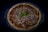 A freshly baked pizza topped with sliced red onions, grated cheese, and garnished with a fresh basil leaf at the center. The crust is golden brown, and the pizza is placed in a round baking dish against a dark background.