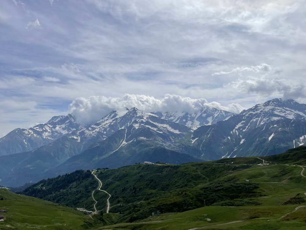 green grass field near snow covered mountain under white clouds during daytime