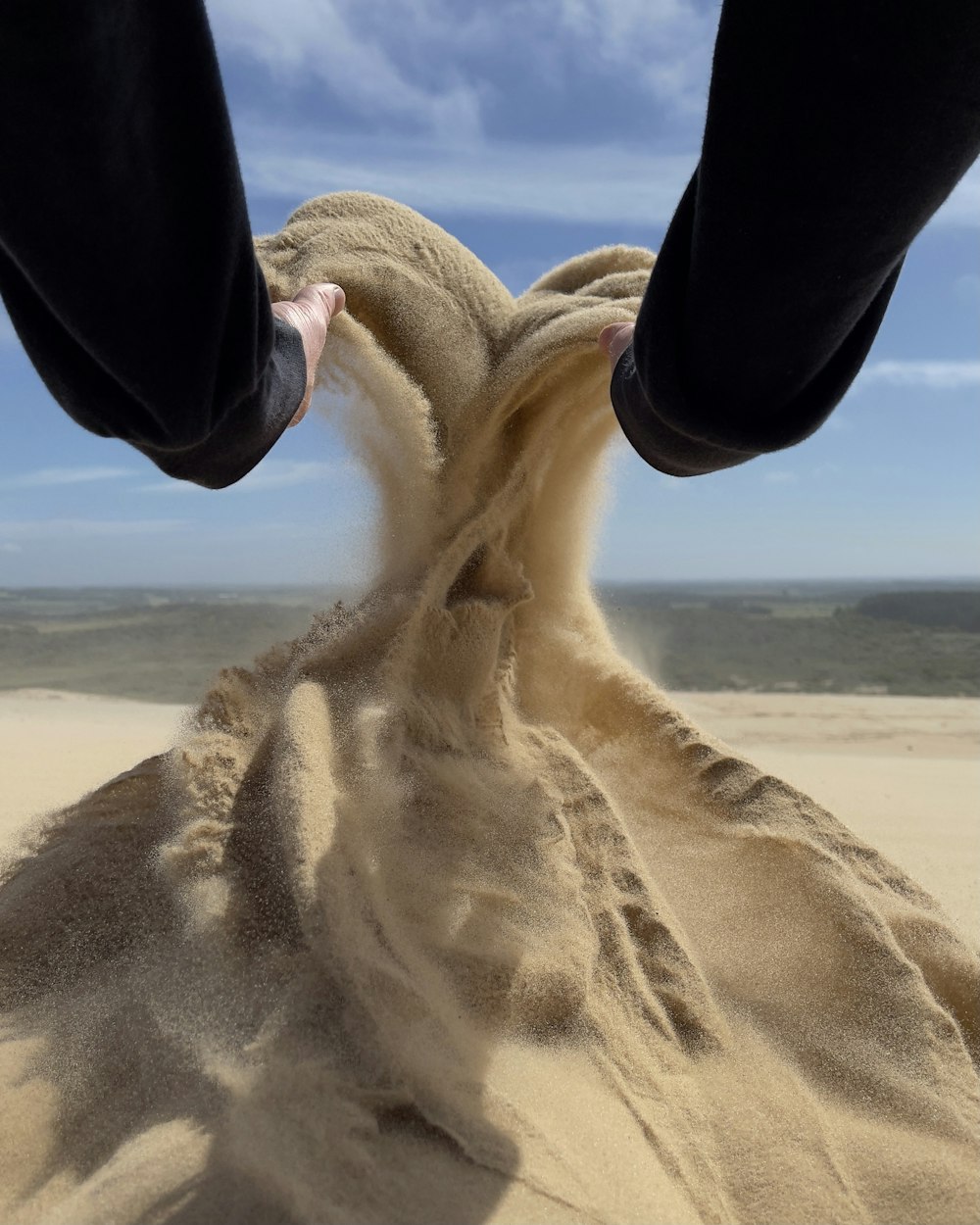 person in black pants sitting on sand during daytime