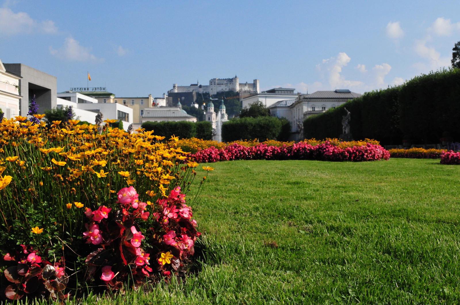 Formal garden with vivid yellow and pink flower beds beside a green lawn.