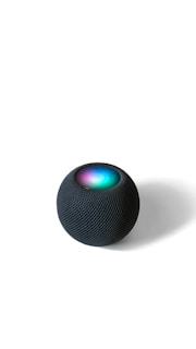 A spherical smart speaker with a mesh-like texture sits on a flat surface. The top of the device exhibits a glowing LED display with vibrant colors including blue, green, and purple.