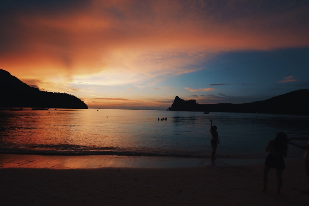 silhouette de personne debout sur le bord de mer pendant le coucher du soleil