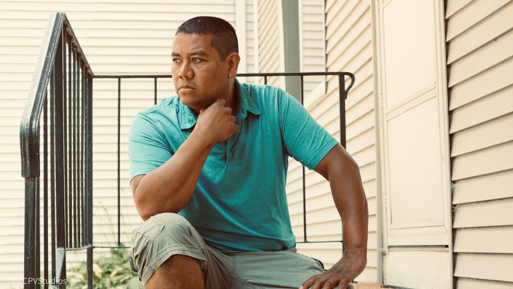 청록색 크루넥 티셔츠를 입은 남자가 흰색 나무 벤치에 앉아 있다
