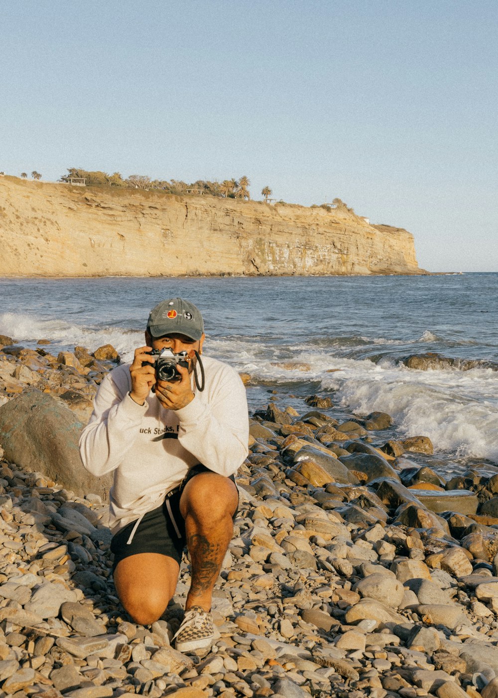 man in white shirt wearing black goggles sitting on rock near sea during daytime