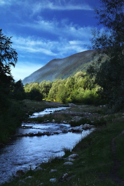 A serene river flowing gently through a lush green valley under a clear blue sky.
