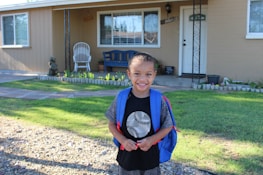 A happy child holding a backpack, ready for school, with a bright smile on their face.