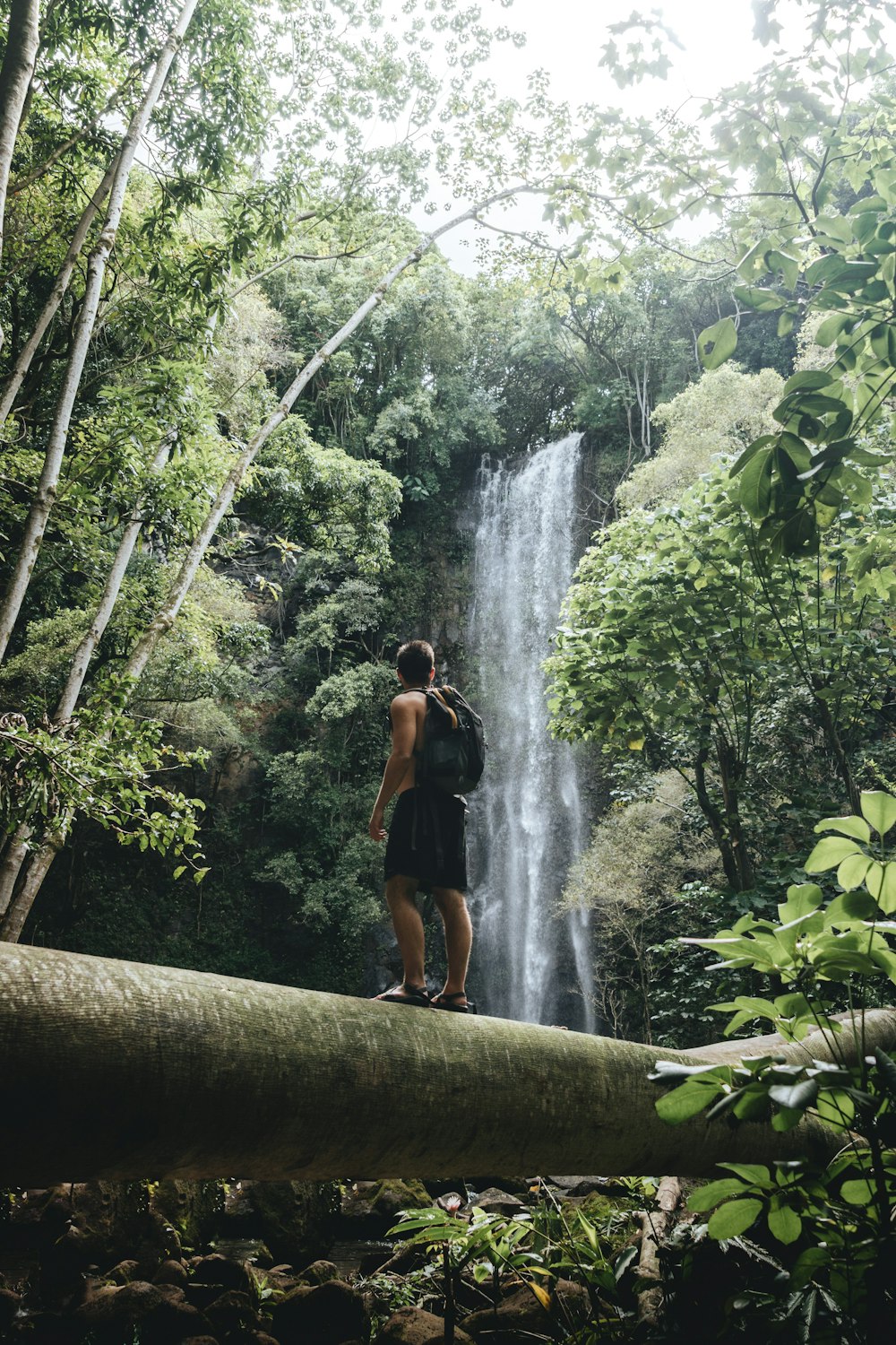 woman in black tank top and black shorts standing on brown wooden bridge near waterfalls during