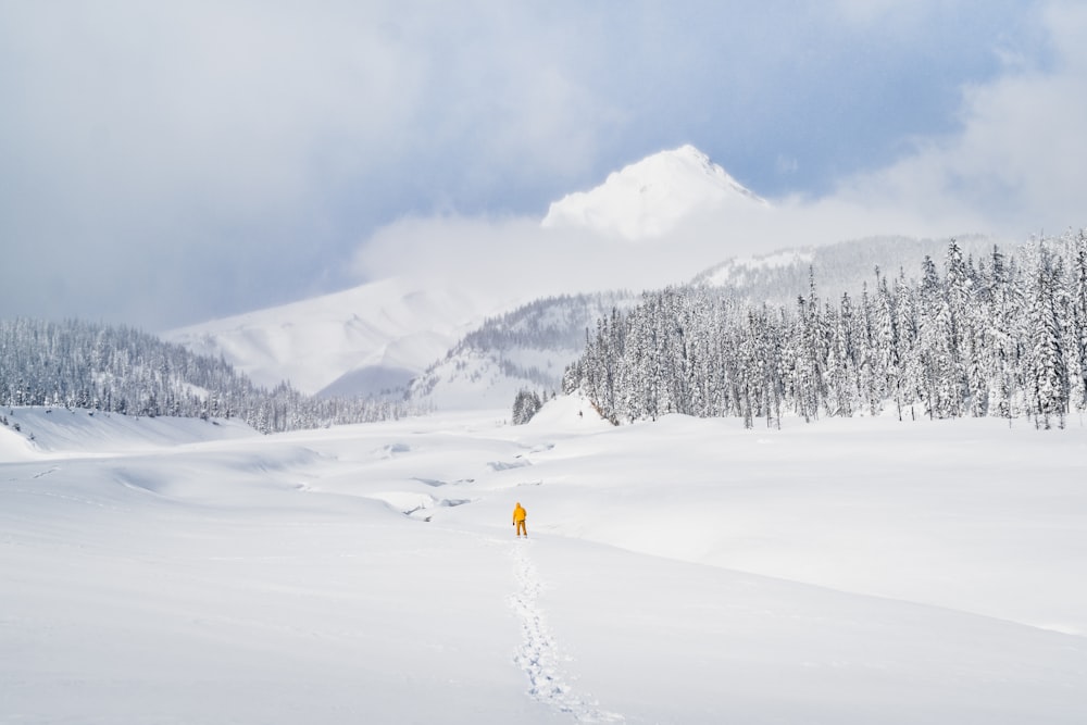 person in yellow jacket and black pants standing on snow covered ground during daytime