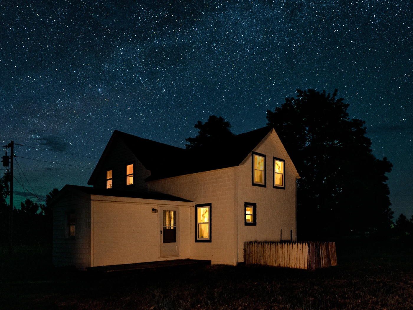 A warmly lit two-story home with glowing windows under a starry night sky