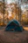 Smiling woman setting up a green Terraviva tent in a forest clearing at dawn