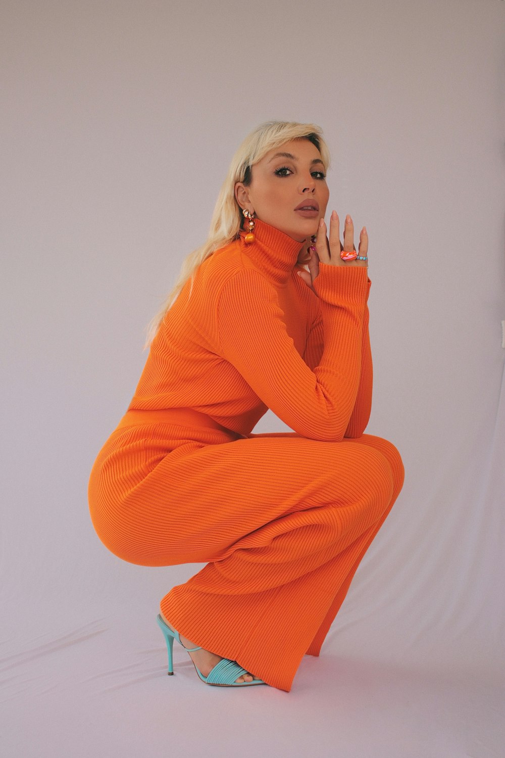 woman in orange sweater and brown pants sitting on white floor