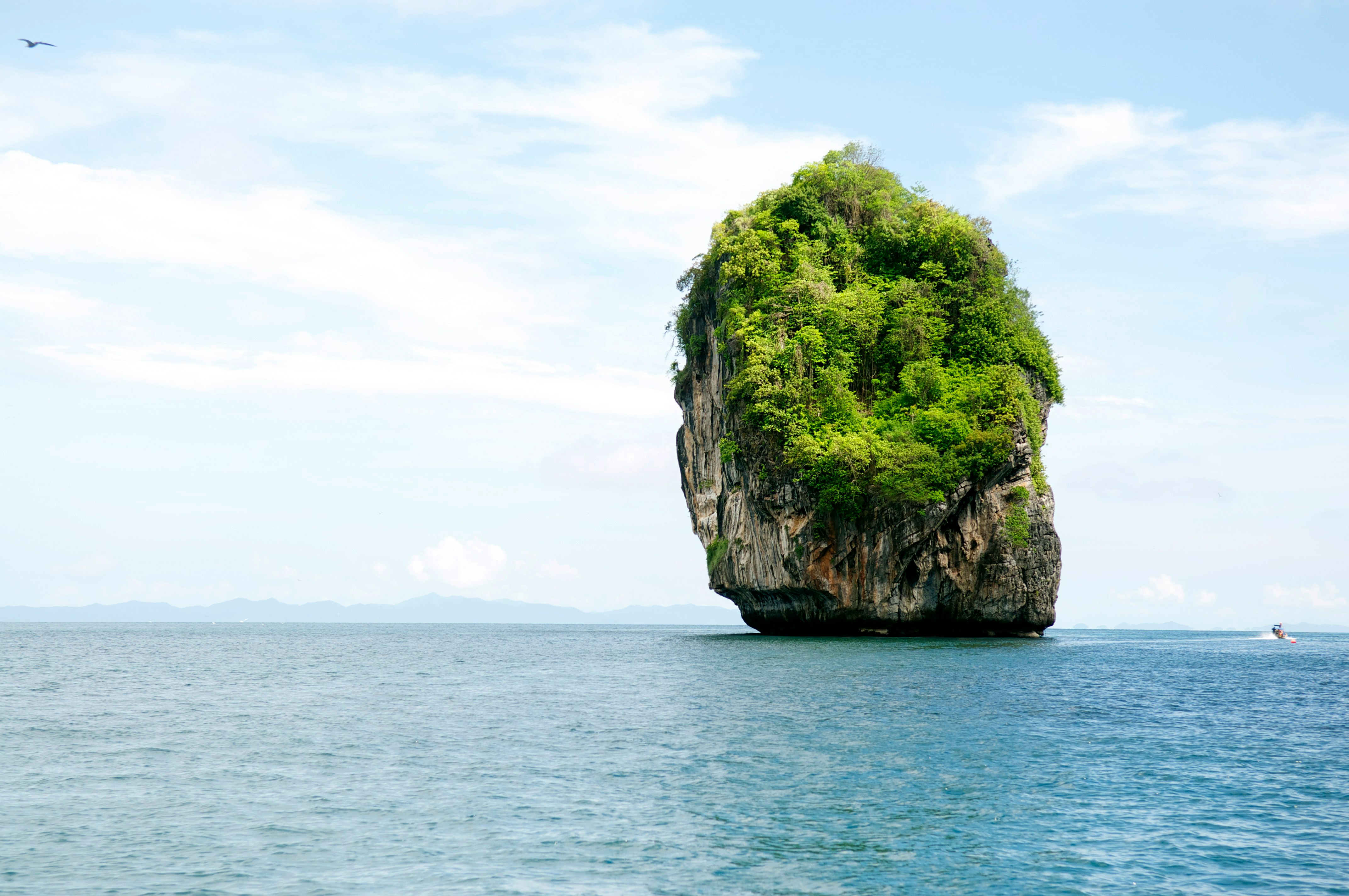 green and brown rock formation on sea under white clouds during daytime