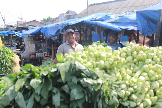 A matte forest green banner hanging outside a bustling local food market, with fresh produce and smiling vendors in the background.