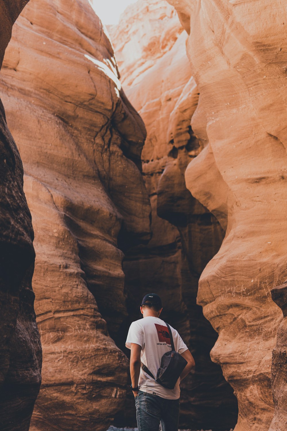 man in white shirt standing in front of brown rock formation during daytime