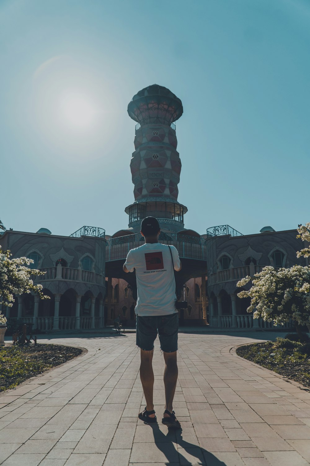 man in white t-shirt and brown shorts standing near brown concrete building during daytime