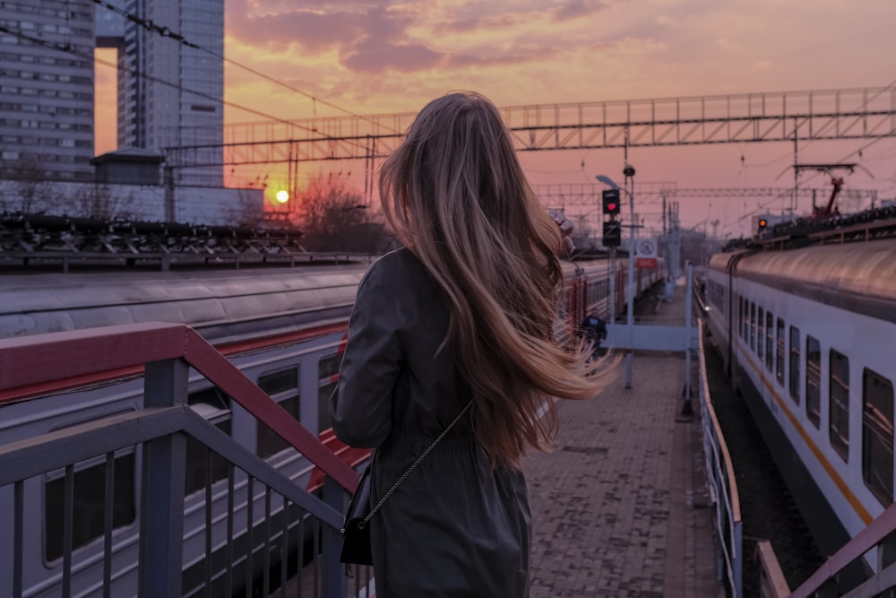 Frau im schwarzen Mantel steht bei Sonnenuntergang auf der Brücke