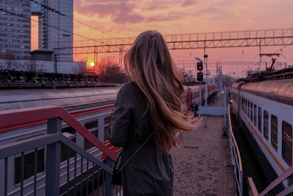 woman in black coat standing on the bridge during sunset