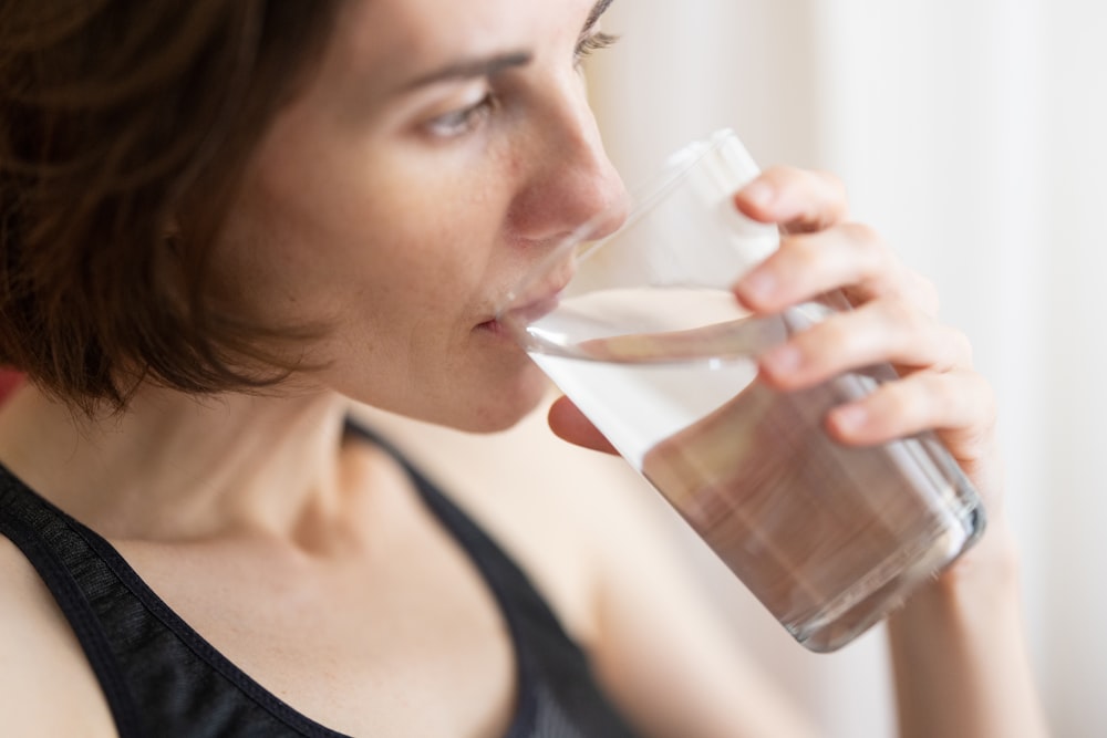 mujer en camiseta sin mangas negra bebiendo agua