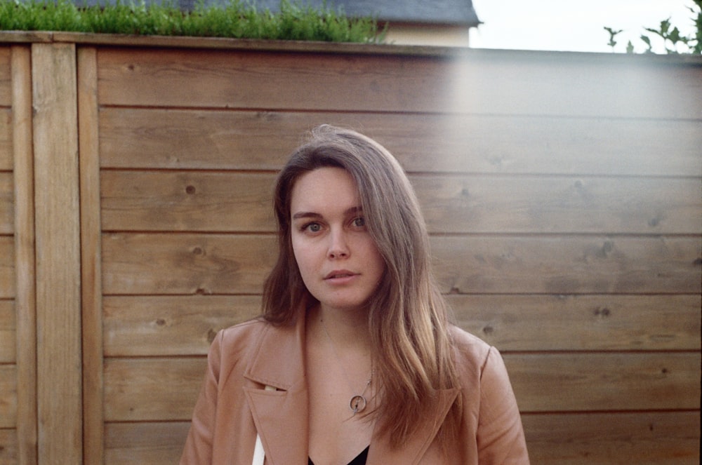 woman in brown coat standing near brown wooden wall