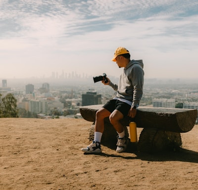 man in gray long sleeve shirt and black shorts sitting on brown wooden bench during daytime