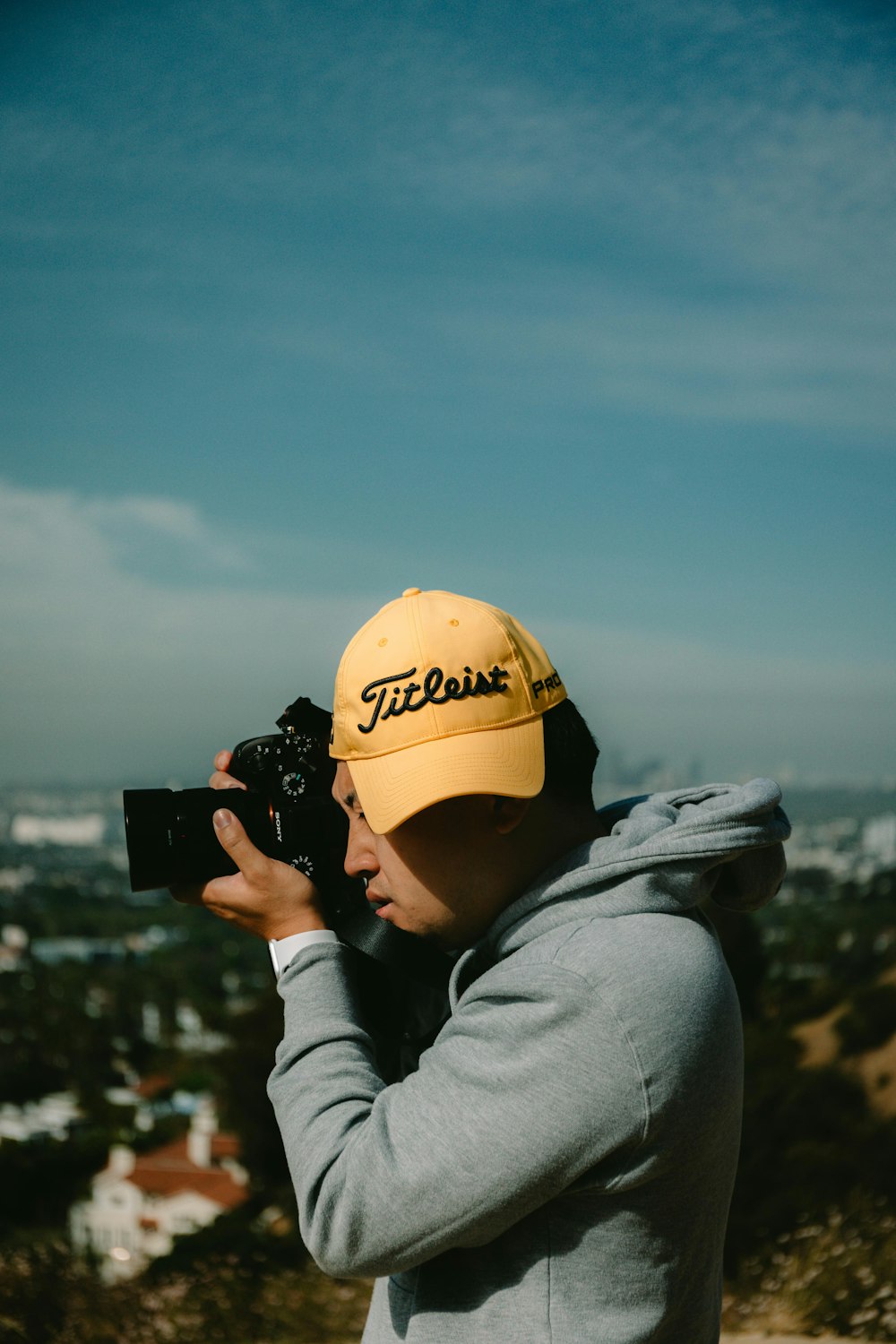 person in yellow cap and gray hoodie holding black dslr camera