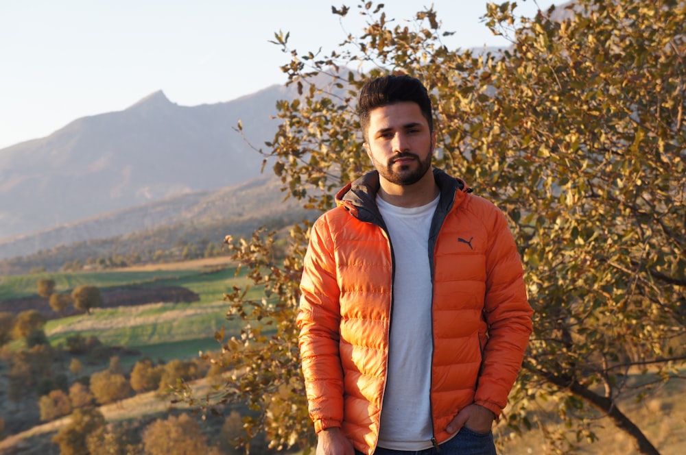 man in red zip up jacket standing near green tree during daytime