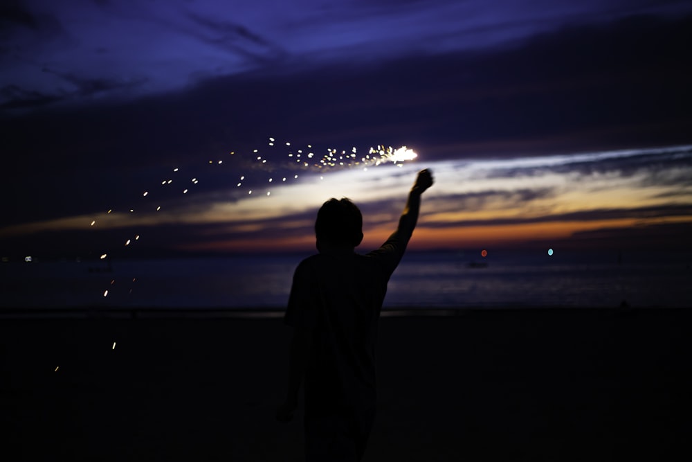 silhouette of man standing on seashore during sunset