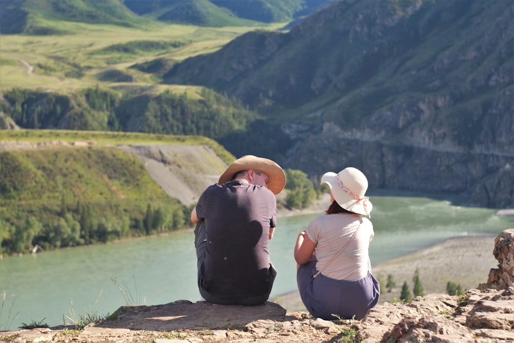 woman in black tank top and white pants sitting on brown rock near lake during daytime