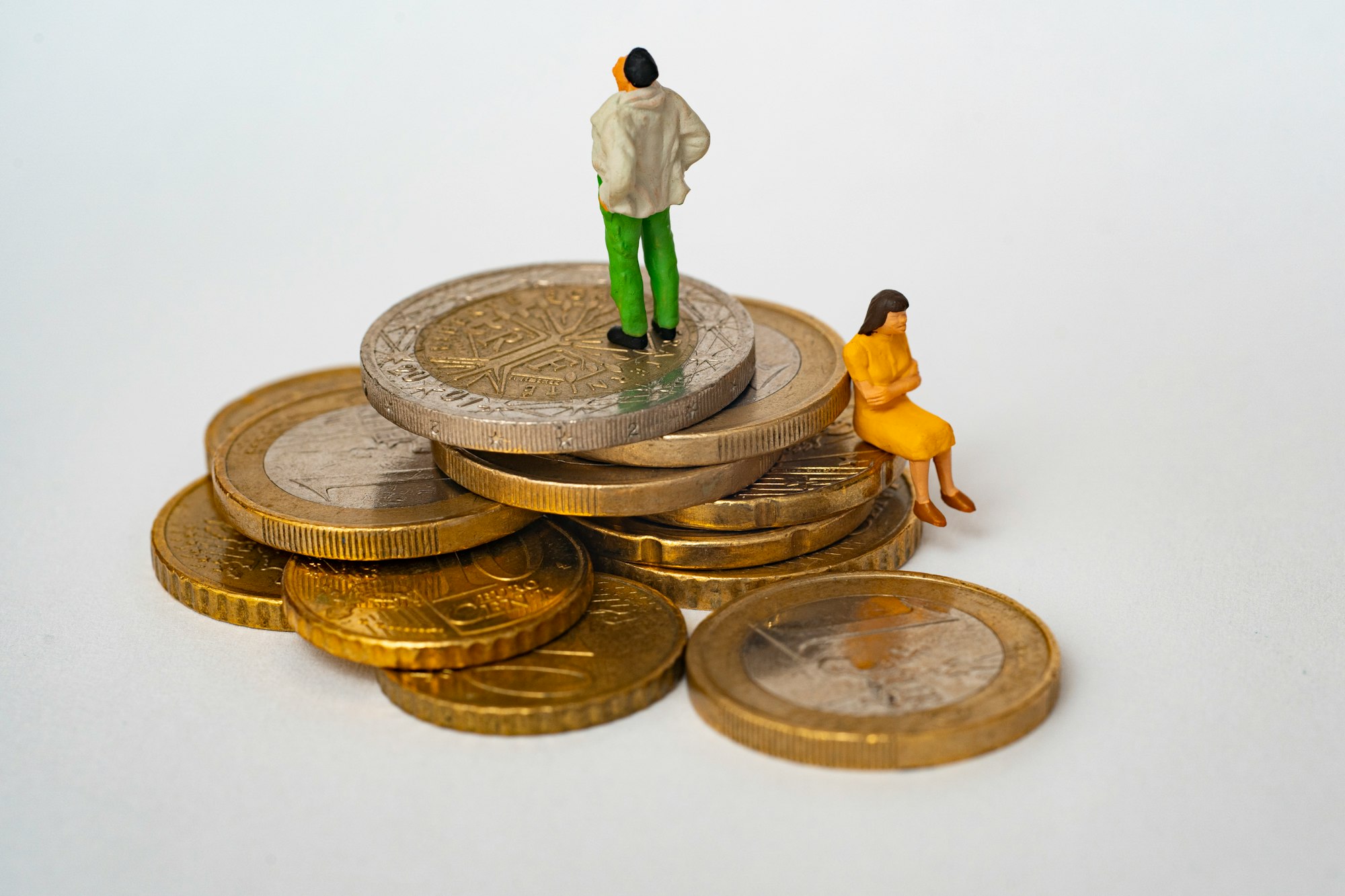 Deux figurines debout et assises sur une pile de pièces de monnaie portant des vêtements de couleur beige, verte et jaune