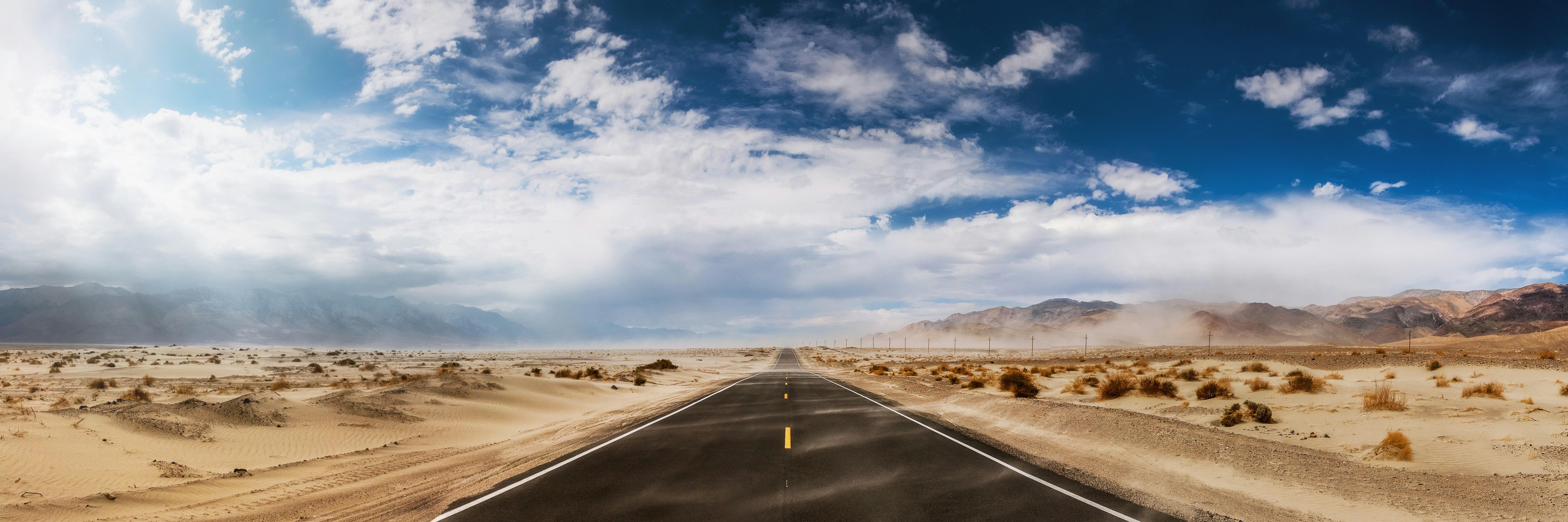 gray asphalt road under blue sky during daytime, Due to the rain falling down on the mountains to the left we where catched in a sandstorm running over the desert tale near Keeler, CA.