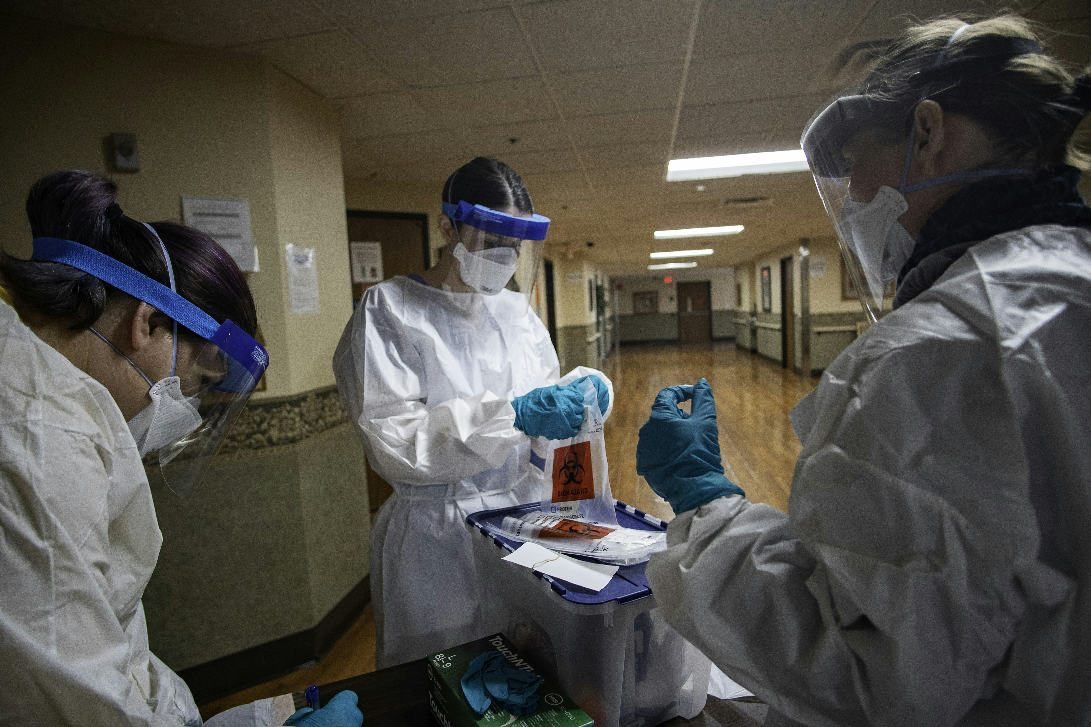 In this April 2020 photo, a team of three volunteers was preparing swabs to test residents of a skilled nursing facility in Detroit, Michigan, for COVID-19. The volunteer at right, would collect the specimen from the resident. The volunteer in the center, would then retrieve and store the specimen in viral transport media, while the member on the left, identified pre-labeled biohazard bags for specimen collection.