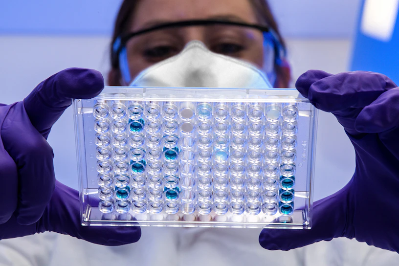 Close-up of a scientist carefully examining a vial of peptide solution under bright laboratory lights.