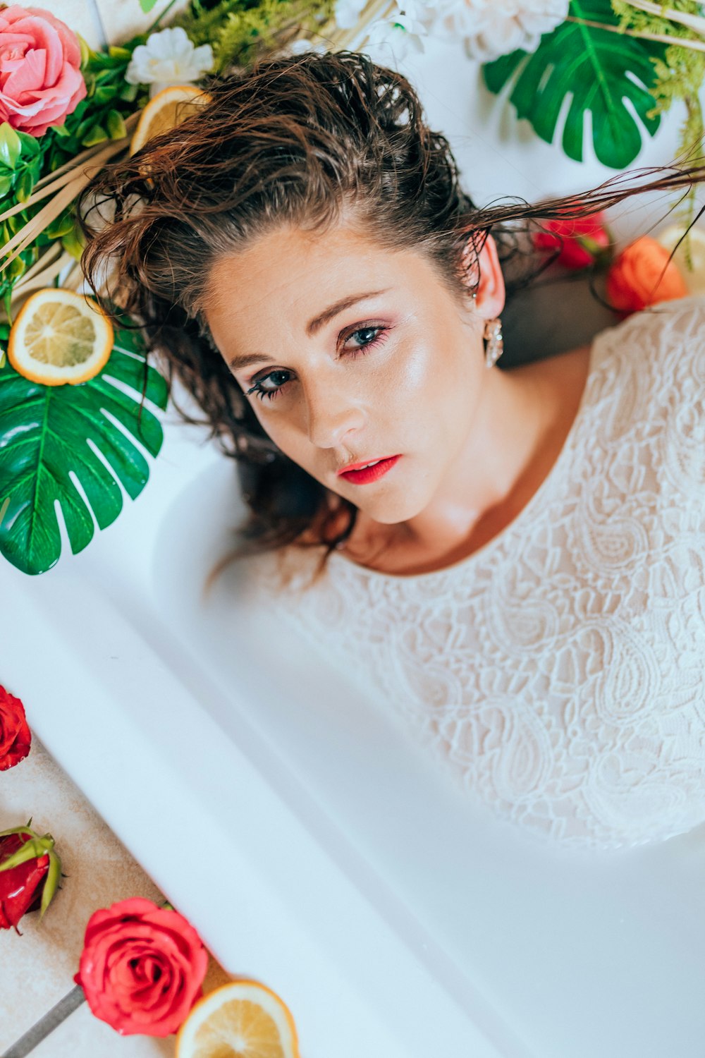 woman in white lace shirt lying on white bathtub with green leaves