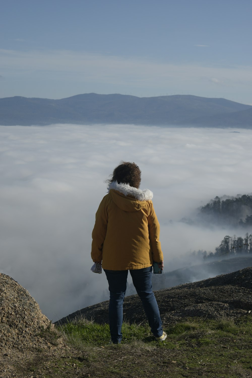 woman in brown jacket and blue denim jeans standing on rock formation during daytime