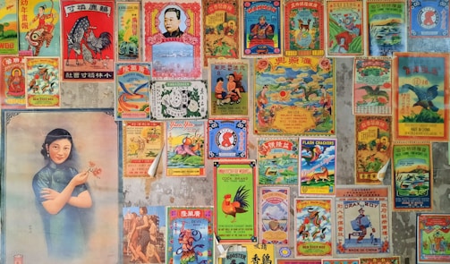 A collage of vintage Chinese posters and advertisements with colorful and intricate designs. The posters feature a variety of images including traditional symbols, animals like roosters and dragons, and a portrait of a woman in a traditional dress holding flowers. The images are arranged tightly together, covering a wall, with an aged and nostalgic aesthetic.
