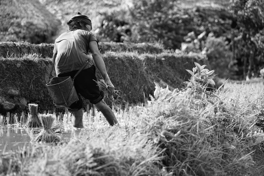 grayscale photo of man in t-shirt and shorts carrying bag walking on grass field