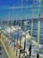 A line of fishing rods is neatly arranged along the railing of a boat, with the ocean and frothy waves visible in the background under a clear blue sky. A few pieces of clothing or towels are draped over the railing.