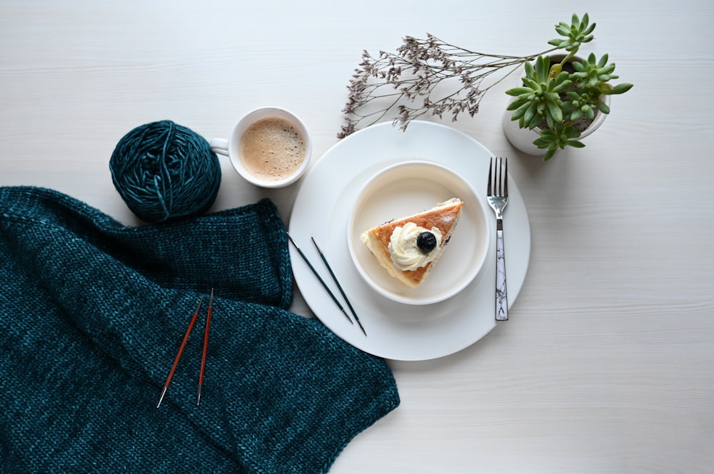 white ceramic mug on white ceramic plate beside blue knit textile