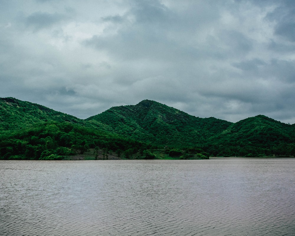 green mountain beside body of water under cloudy sky during daytime
