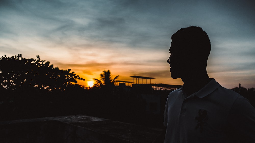 silhouette of man standing near trees during sunset