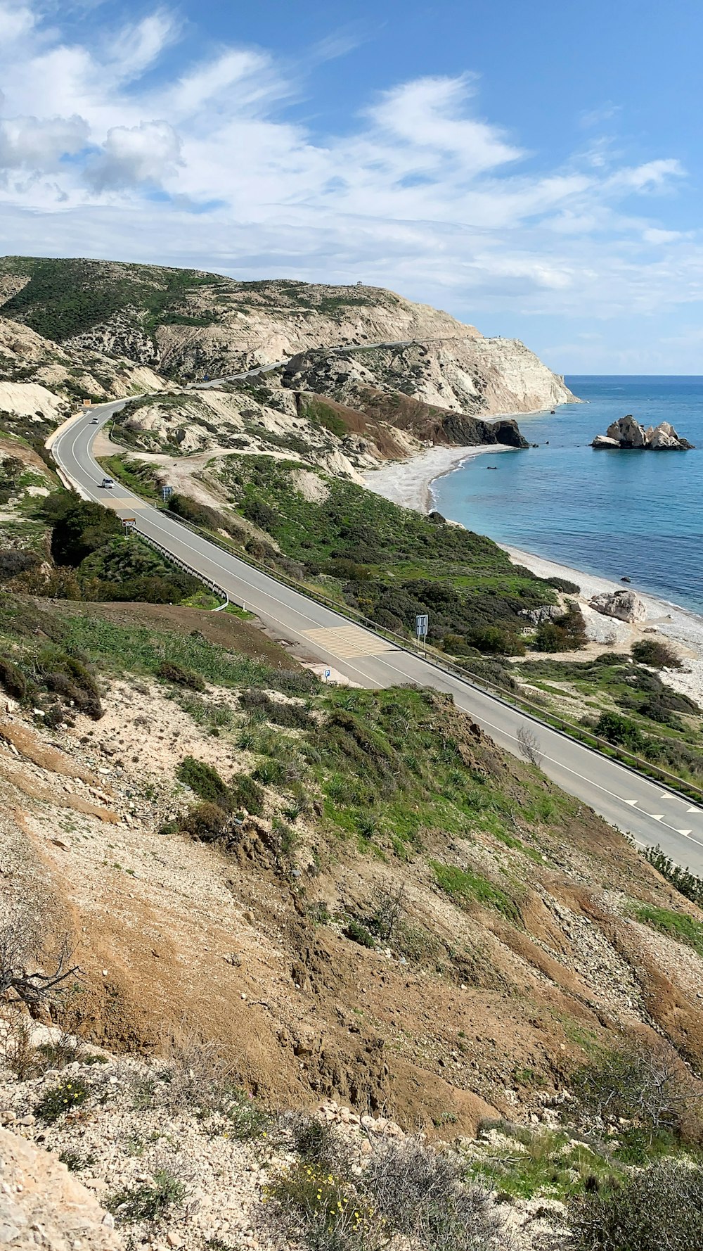 gray asphalt road on mountain near body of water during daytime