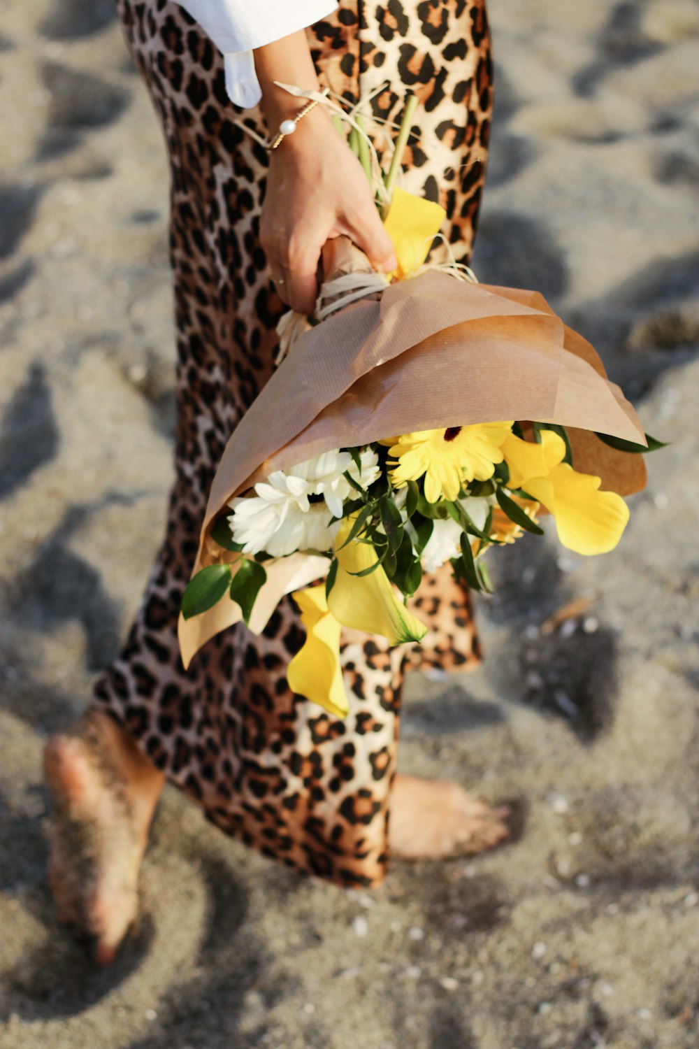 Personne en pantalon imprimé léopard marron et noir tenant des fleurs jaunes