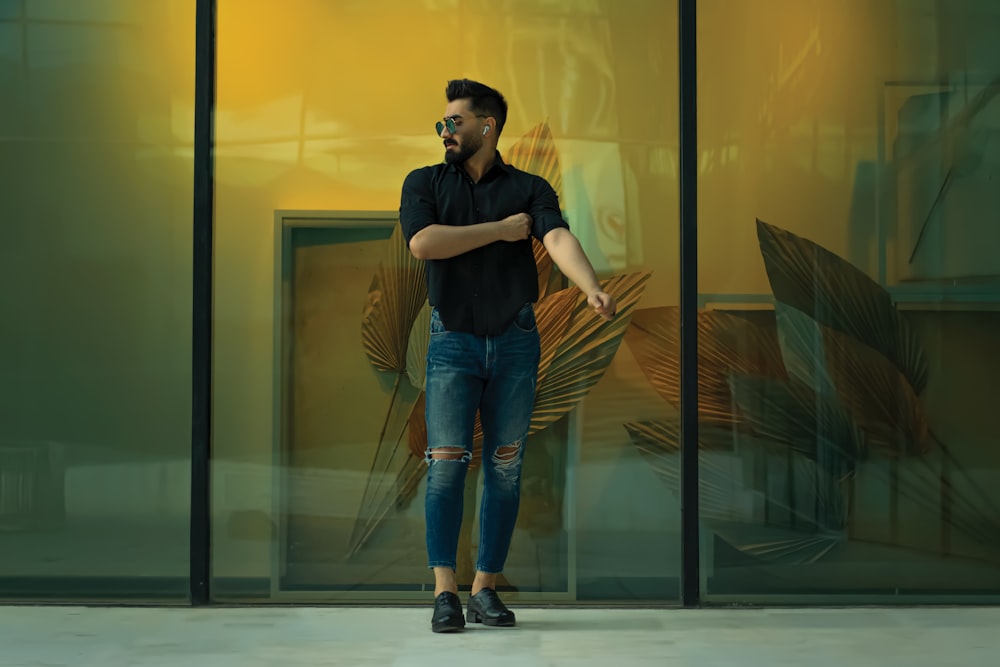 woman in black tank top and blue denim jeans standing beside glass wall