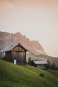 brown wooden house on green grass field near brown mountain during daytime