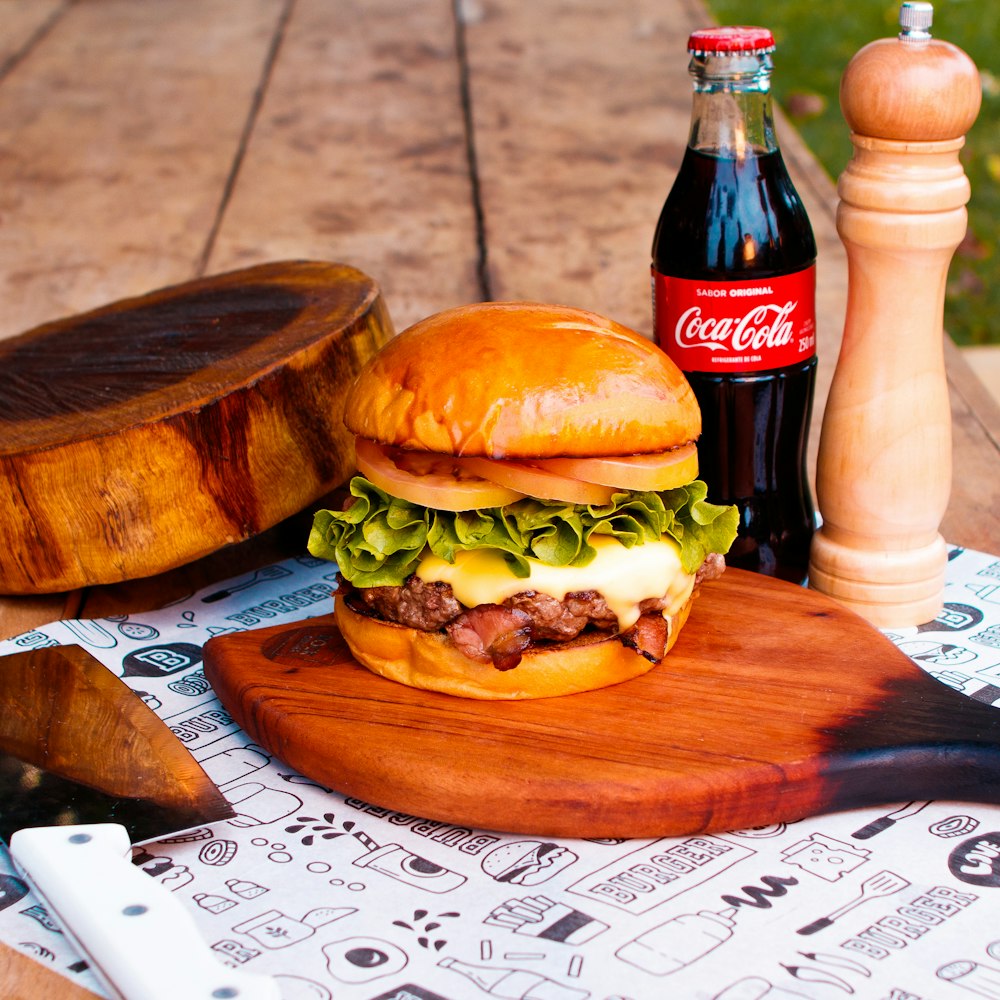 a hamburger sitting on top of a cutting board next to a bottle of coke