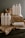 A collection of white plastic cleaning bottles with black text, arranged on crumpled brown paper and a dark wooden surface. The bottles have various labels such as 'Glass Mirror Steel Tincture' and 'Floor Concentrate Tincture.' The background is a plain gray wall.