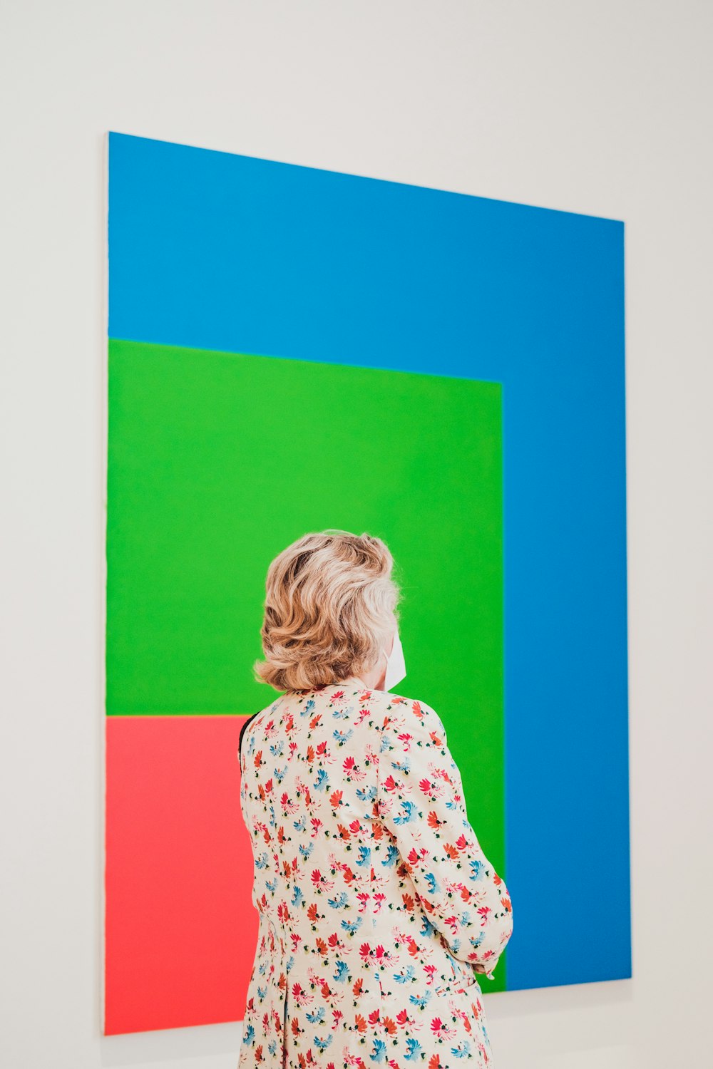 girl in white and red floral long sleeve shirt standing beside blue orange and green wall