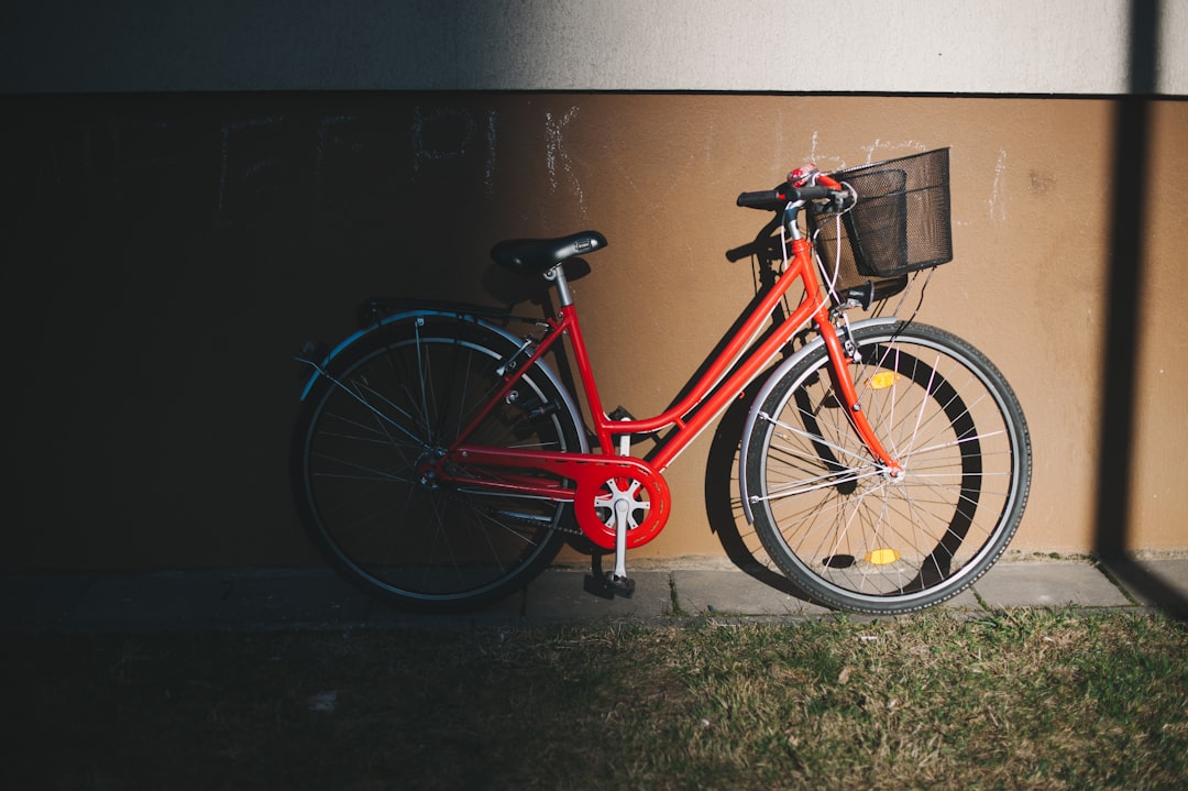 red city bicycle parked beside gray wall