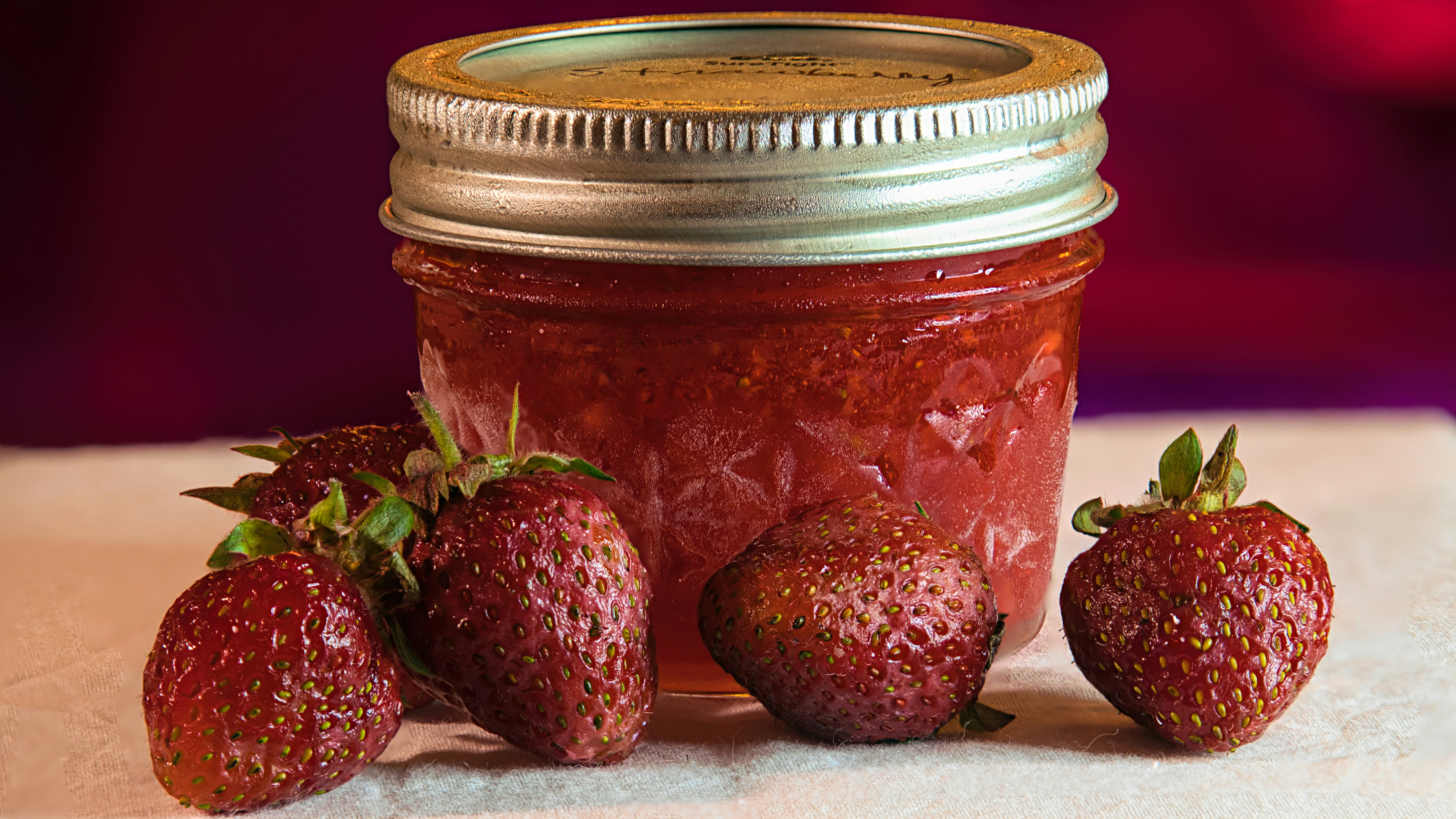 Beautiful ruby red strawberry jam in a glass jar with fresh strawberries on a rustic table