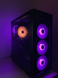 A computer case with a transparent side panel displays illuminated cooling fans. The fans emit a vibrant purple light, with one prominent fan on the left glowing orange. The case is situated against a plain background, enhancing the striking contrast of the lighting.